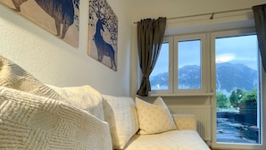 A cozy living room with a beige sofa, two wall-mounted paintings, and a window with a view of mountains. - Haus Sabine (Leutasch)