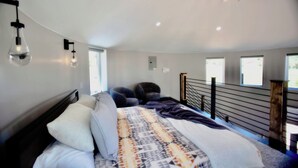 A modern bedroom with a curved ceiling, a bed with patterned bedding, two wall-mounted light fixtures, and a ceiling fan. - The Silo Loft at Goose Lake Lane, at East Zion & Bryce Canyon National Parks (Glendale)