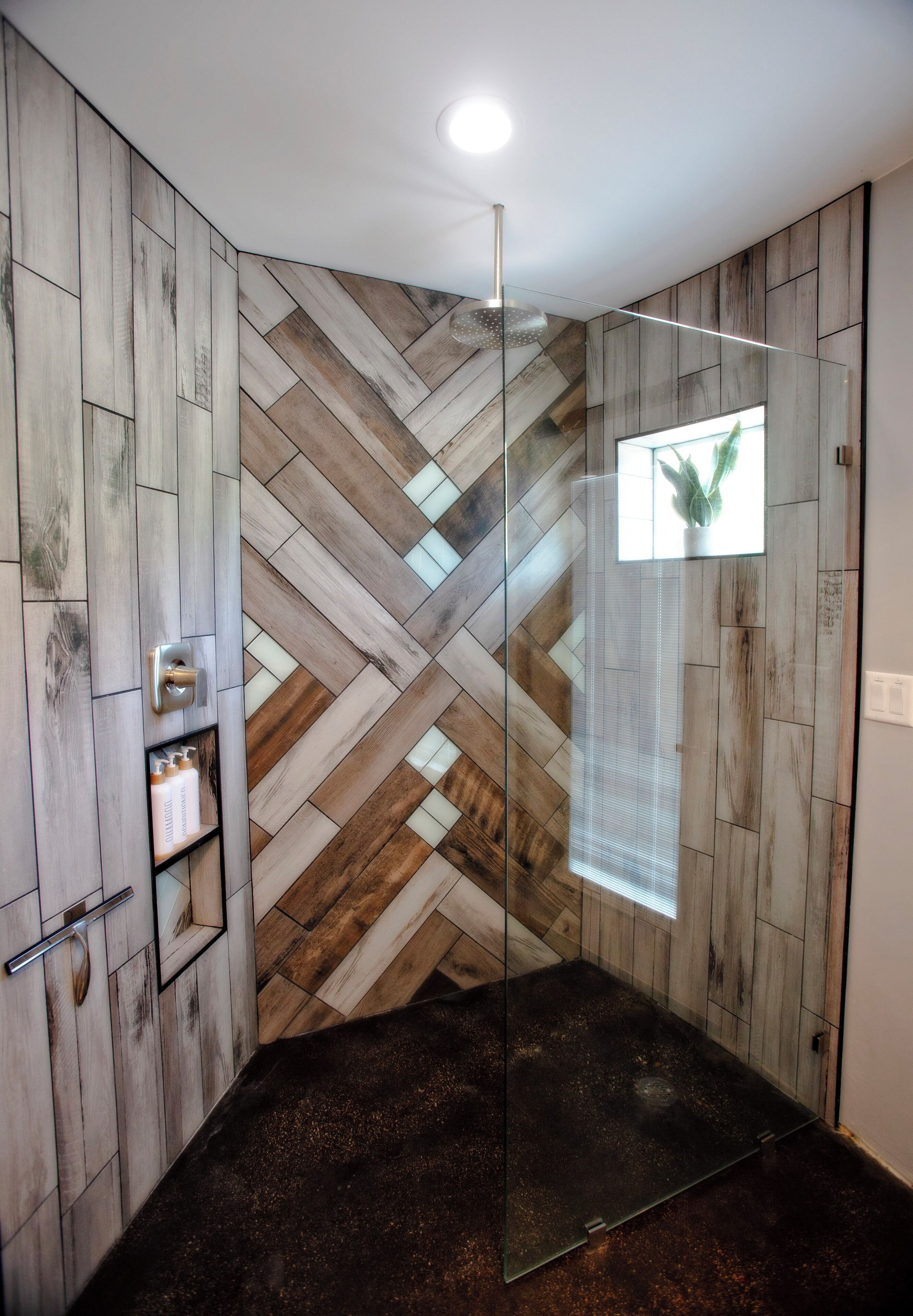 Ein modernes Badezimmer mit Wandverkleidung aus Holz-Fischgrätmuster, einer Duschkabine aus Glas und einer integrierten Ablage für Toilettenartikel.