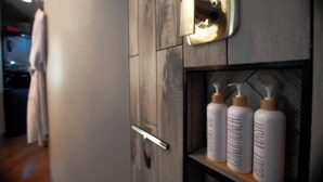 A bathroom with wooden paneling, a towel rack, and three bottles of lotion on a shelf. - The Silo Loft at Goose Lake Lane, at East Zion & Bryce Canyon National Parks (Glendale)