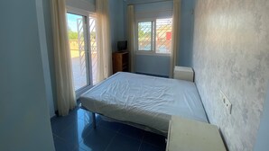 Un dormitorio con cama, un televisor sobre un soporte de madera y una ventana con cortinas.