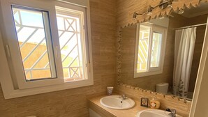 Un baño con dos lavamanos, un inodoro, un bidé y una ventana que ofrece vistas a un edificio amarillo.