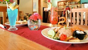 A dining table with a plate of food, two drinks, and a vase with flowers. - Seashell Suite, Garden & Pool Views @SapphireBeach (San Pedro Town)