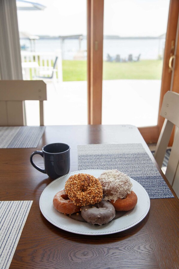 A plate of assorted donuts on a table with a blue placemat, a dark mug, and a view of a grassy area through a glass door.