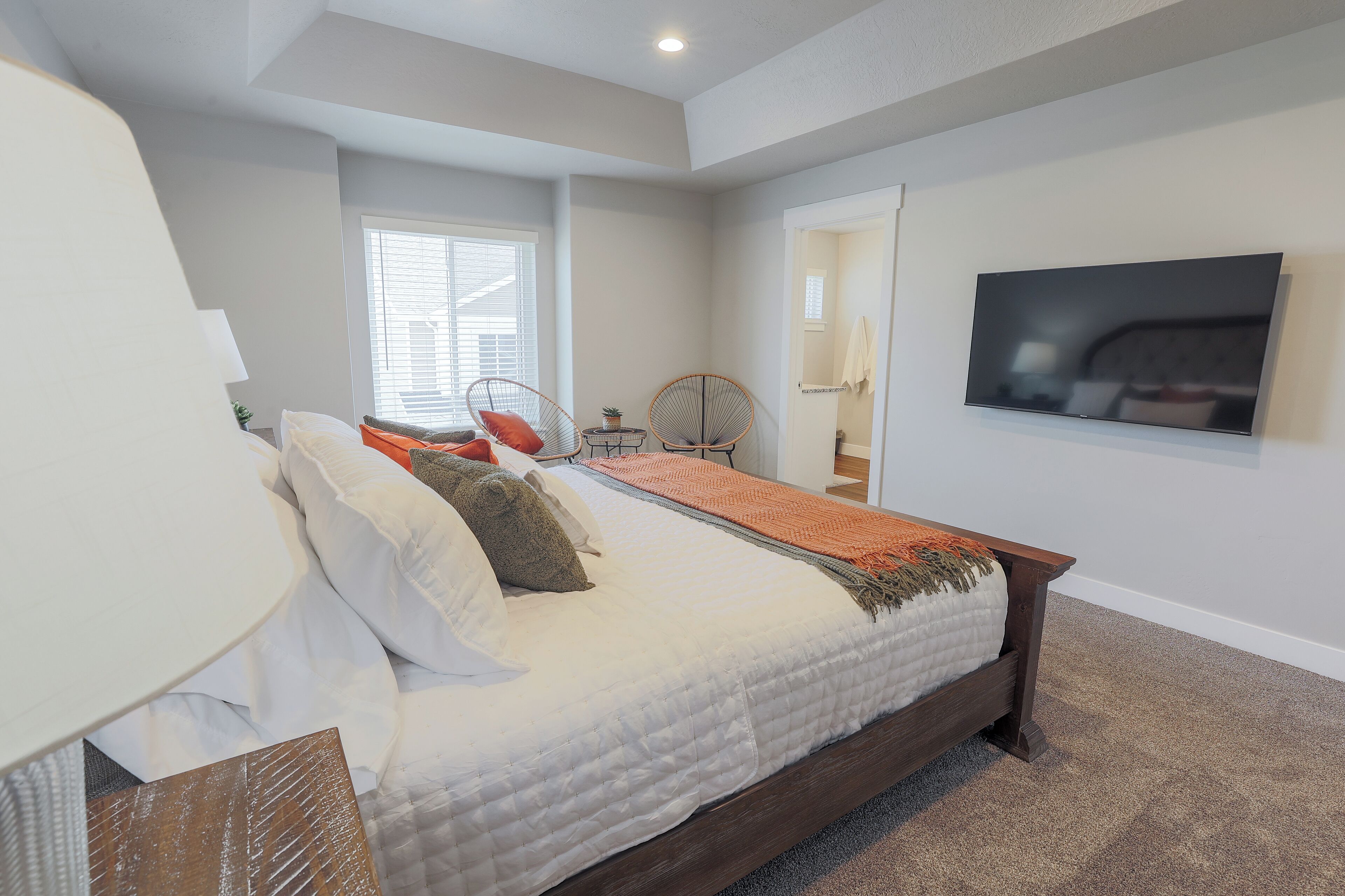 A bedroom with a large bed, a TV mounted on the wall, and a window with blinds.