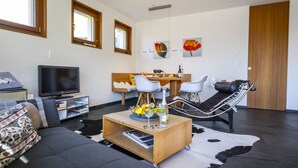 Ein modernes Wohnzimmer mit einer Couch, einem Couchtisch mit Früchten und Getränken, einem Fernseher und einem Essbereich mit Stühlen und Tisch.