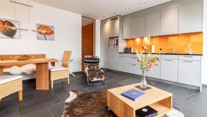 Ein modernes Wohnzimmer mit einem Holzespeisetisch, einer Couch und einem einzigartigen Schaukelstuhl aus Rindsleder. In der Mitte steht ein kleiner Holztisch mit einer Blumenvase.