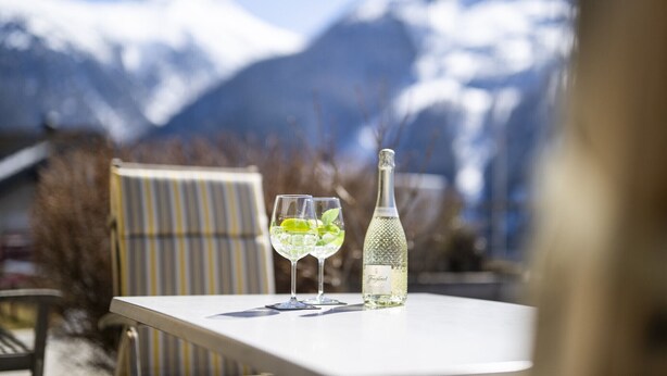 Ein Tisch mit zwei Gläsern und einer Flasche, vor einer Bergkulisse.