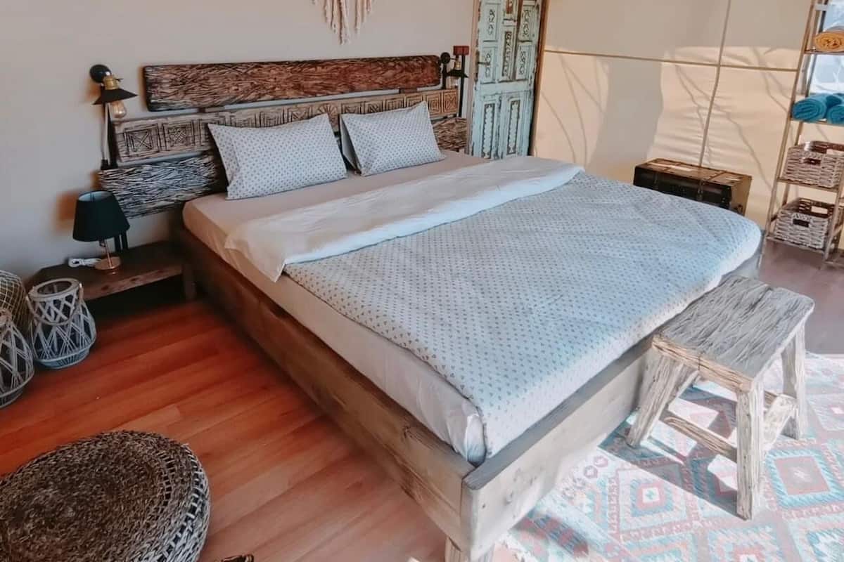 A cozy bedroom with a wooden bed, a woven bench, and a patterned rug.