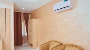 Een kamer met een beige wand, een houten garderobe, een beige bank en een airconditioner.