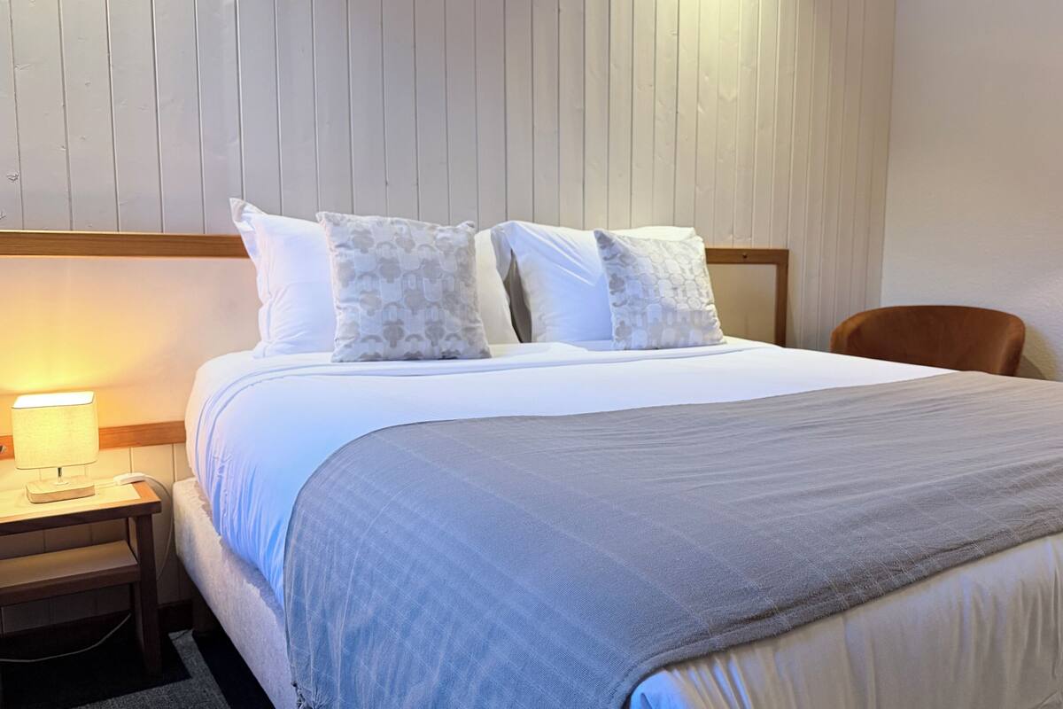 A neatly made bed with a grey blanket, a wooden headboard, and a bedside lamp.