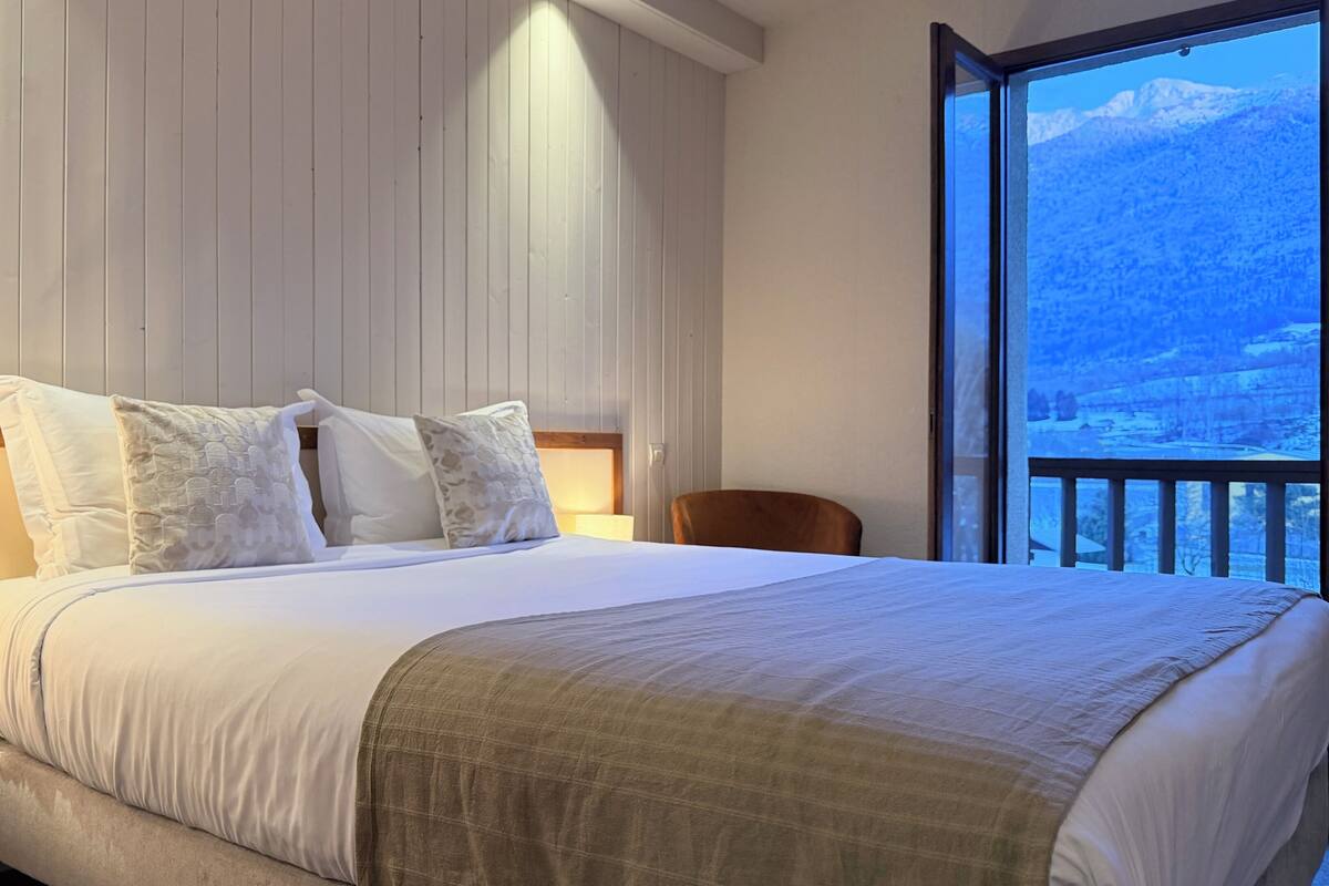 A bed with a wooden headboard, a bedside lamp, and a view of a snowy mountain through a balcony.