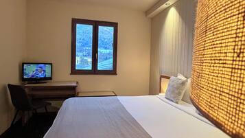 A hotel room with a bed, a desk with a television, and a window with a view of a snowy landscape.
