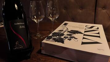 A bottle of Audacieuse St-lean de-la-Porte wine, two empty wine glasses, and a book titled 'VINs' on a wooden table.