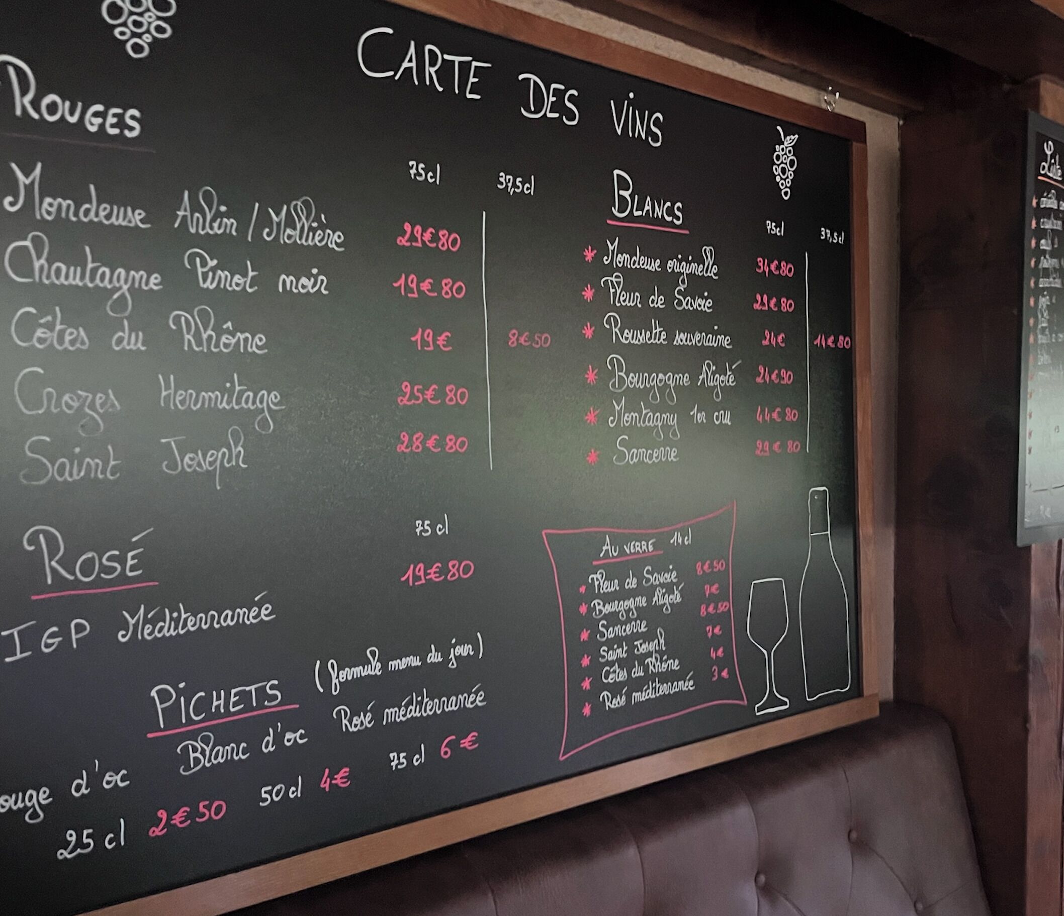 Pizarra con menú que enumera varios vinos y platos, junto con sus precios.
