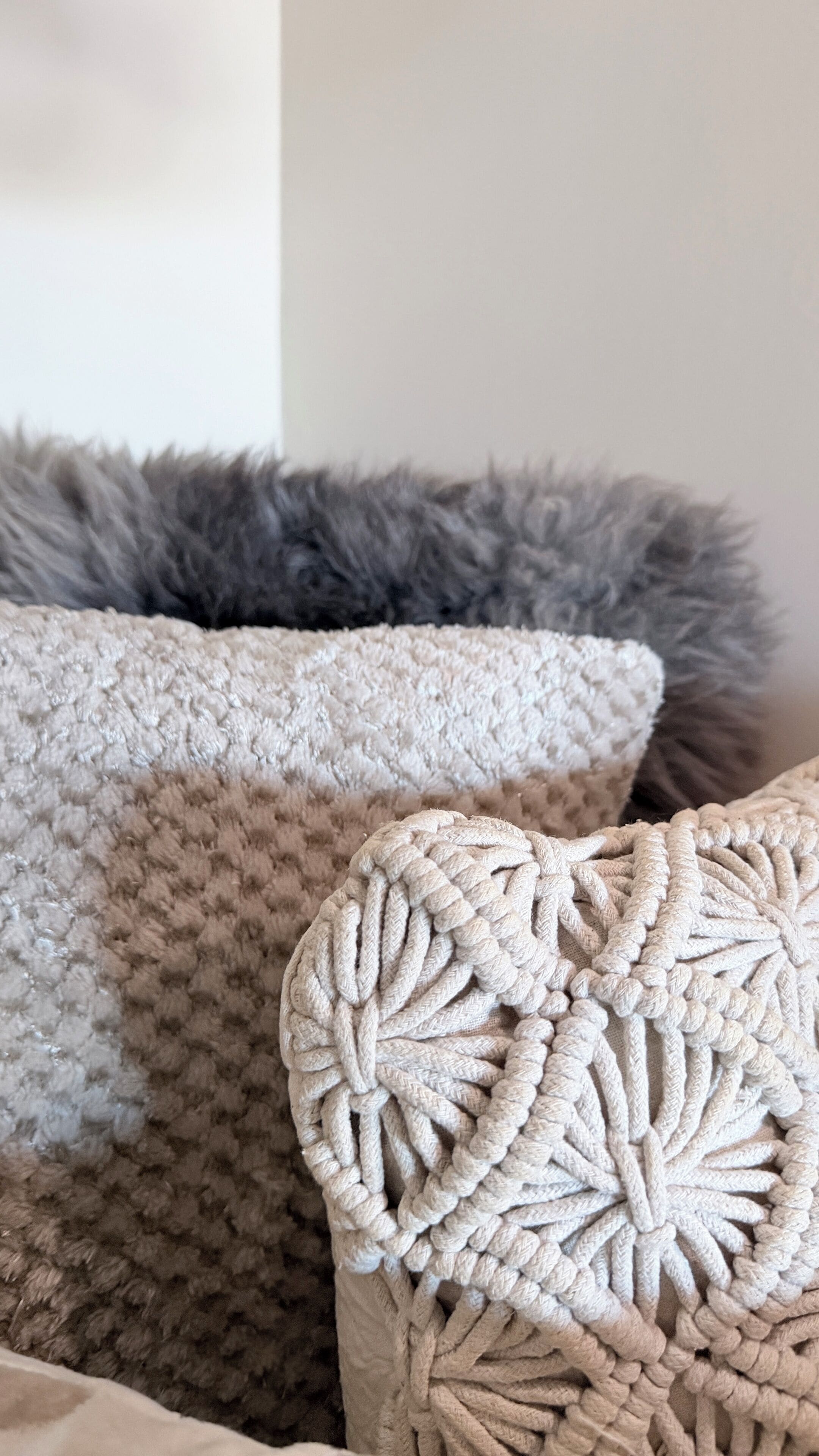 A close-up of a textured, knitted pillow with a heart-shaped design, placed on a bed with a fluffy, grey blanket.