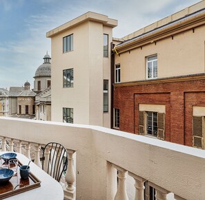 Un balcon avec une table et des chaises, donnant sur un paysage urbain composé d’immeubles aux styles architecturaux variés.