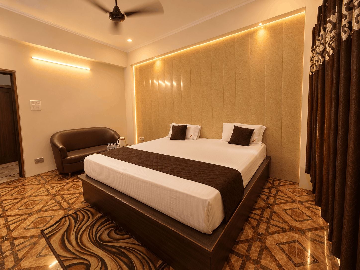 A hotel room with a large bed, a sofa, a ceiling fan, and a patterned floor.