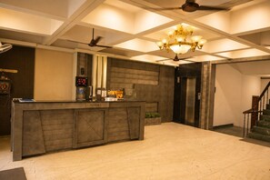 A reception area with a reception desk, a digital clock, a chandelier, and an elevator. - Mansarovar Hotel & Banquets (Bareilly)