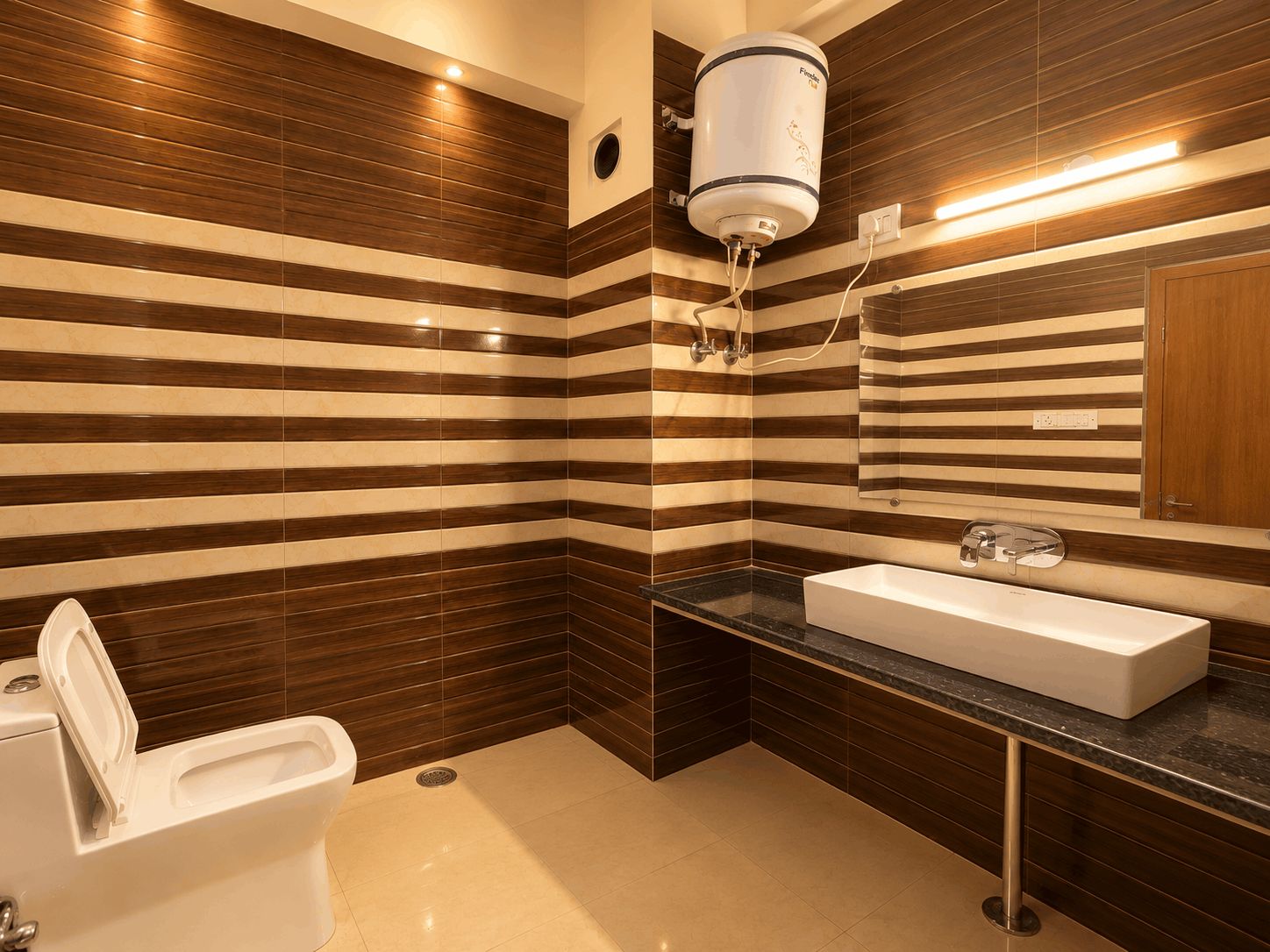 Un baño con inodoro blanco, un lavabo rectangular y un espejo encima. Las paredes tienen un diseño a rayas.