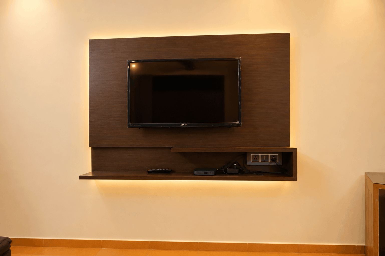 A wall-mounted television with a wooden panel design, a remote control, and a power strip below.