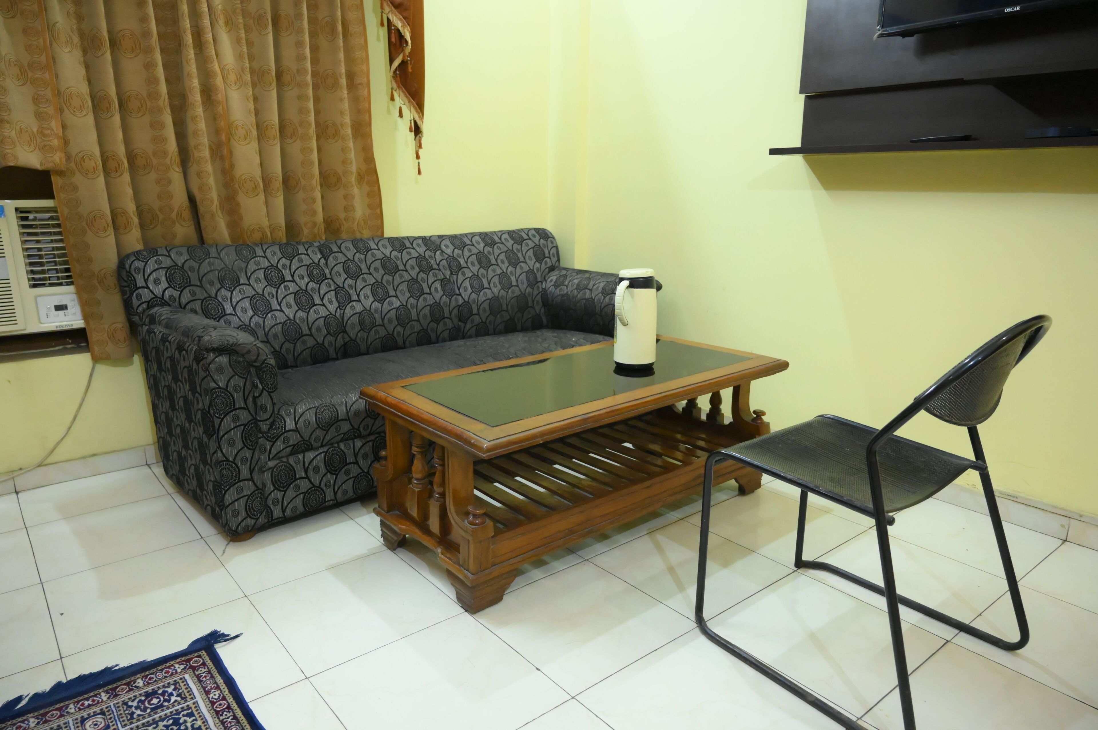 Una sala de estar con un sofá estampado, una mesa de centro de madera, una silla de metal negro y un televisor montado en la pared.