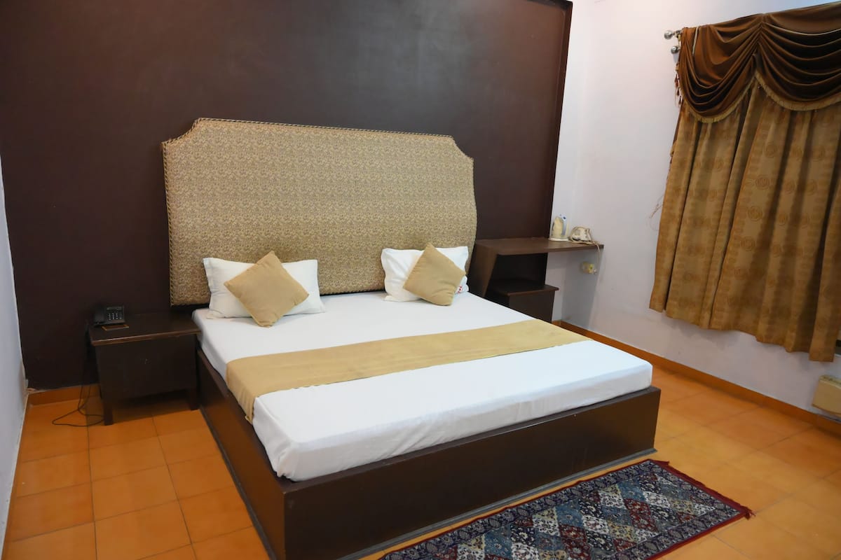A neatly made bed with a headboard, a bedside table with a phone, and a patterned rug on the floor.