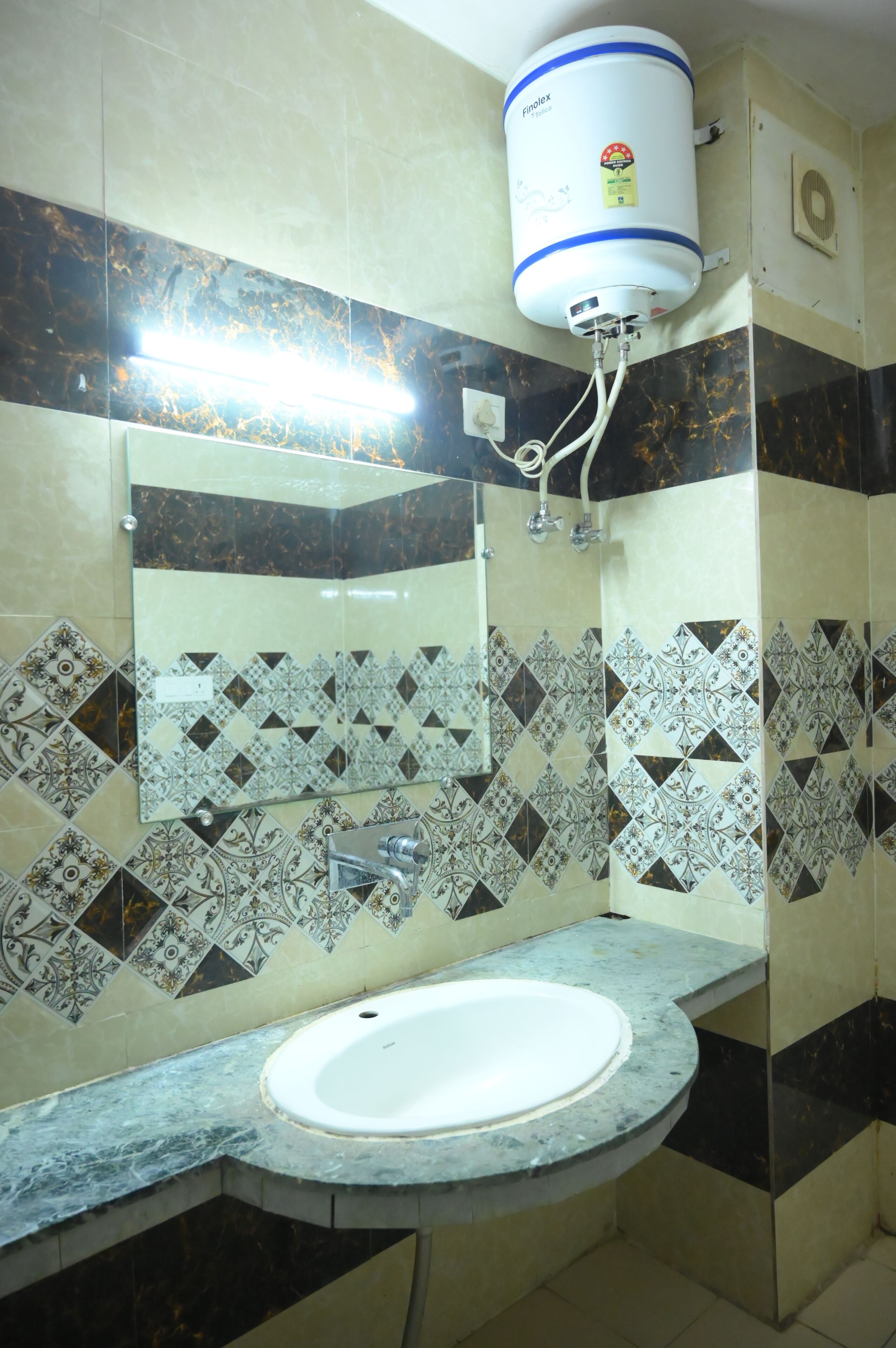 A bathroom with a white sink, a mirror, patterned tiles, and a water heater mounted on the wall.