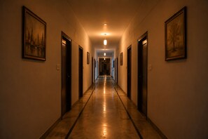 A hotel corridor with doors on both sides, a polished floor, and framed pictures on the walls. - Mansarovar Hotel & Banquets (Bareilly)