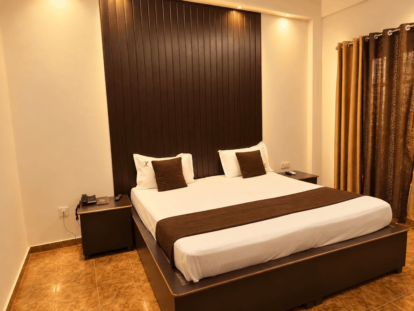 Una habitación de hotel con una cama grande, una mesita de noche, un control remoto y una cortina.