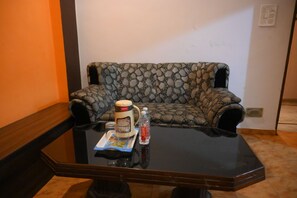 A room with a patterned sofa, a coffee maker, a tray with food, and a water bottle on a glass table.