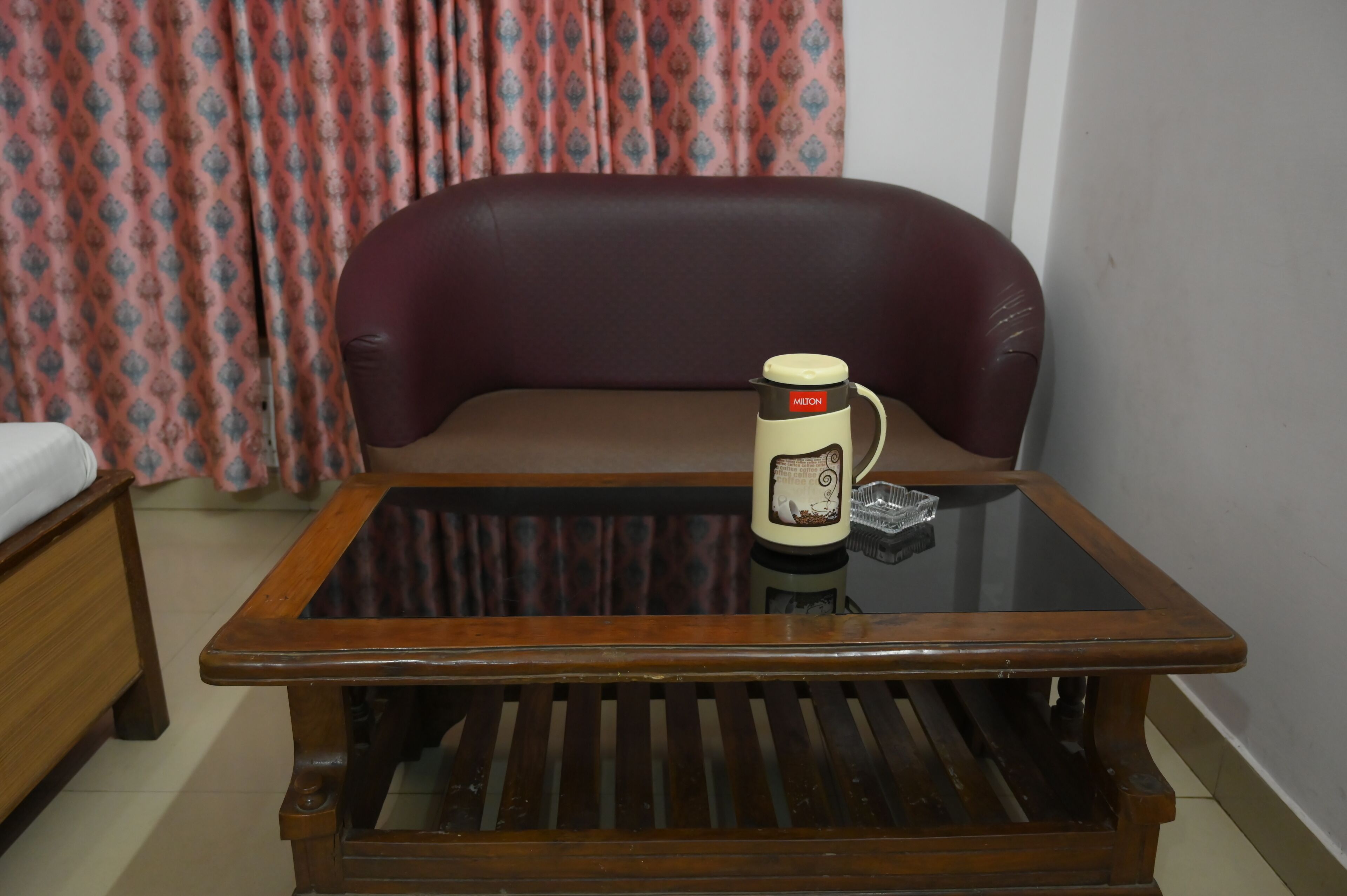 A room with a glass-top coffee table, a brown leather sofa, and a patterned curtain.
