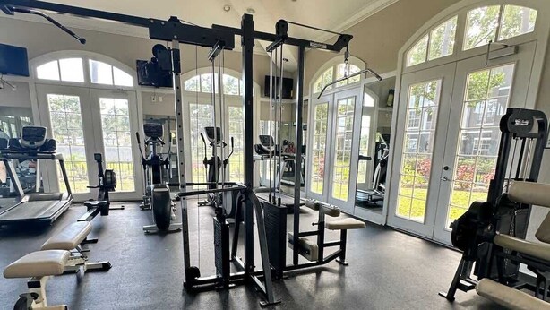 A gym with various exercise equipment, large windows, and a high ceiling. - Crescent Palms - Near Brandon, Tampa, Riverview (Tampa)
