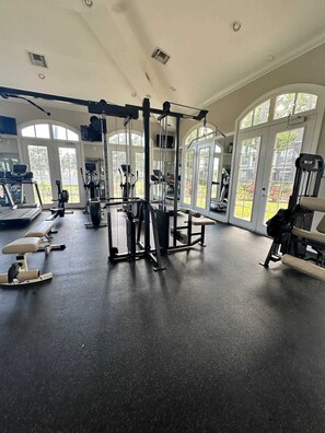A gym with various exercise equipment, large windows, and a high ceiling.