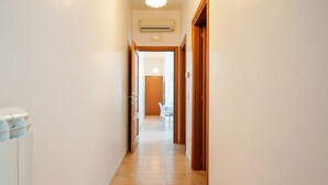 A narrow hallway with a tiled floor, an air conditioning unit mounted on the wall, and a door leading to a room with a table and chairs. - Appartamento a Torre Canne con Balcone (Fasano)