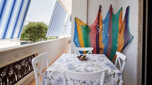 A balcony with a table and chairs, a colorful woven wall hanging, and a view of greenery. - Appartamento a Torre Canne con Balcone (Fasano)
