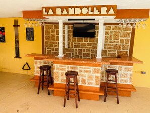 A bar area with a stone wall, a TV mounted above the bar, and three stools.