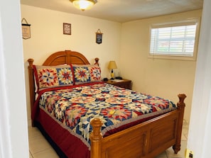 A neatly made bed with a wooden headboard, a bedside table with a lamp, and a window with blinds.