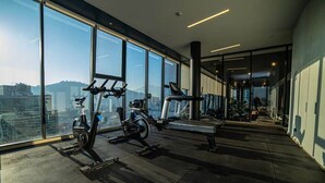 Un gimnasio con equipamiento cardiovascular y ventanas amplias que ofrecen vistas a la ciudad.