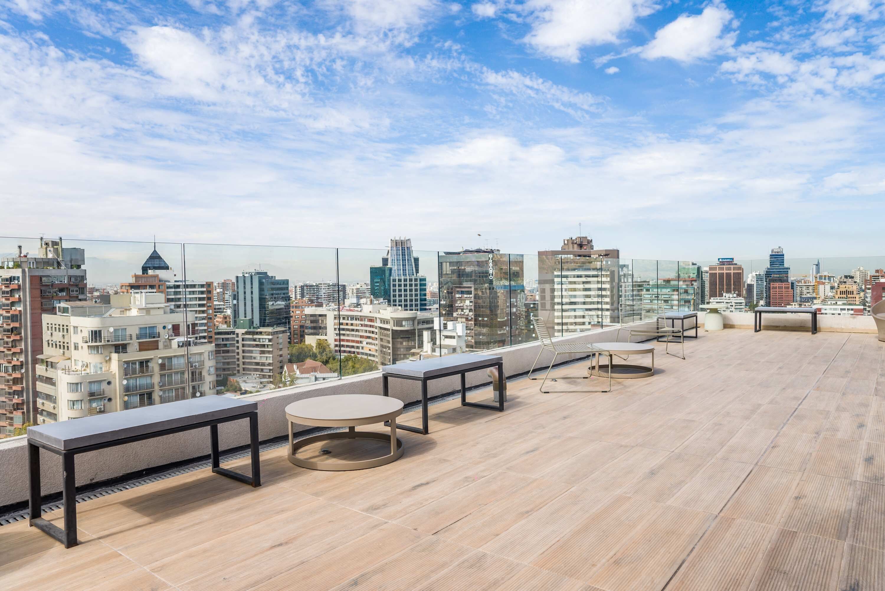 Terraza en la azotea con vistas a la ciudad, que incluye una mesa redonda, un banco y una pequeña mesa.