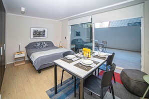 Une chambre d’hôtel moderne, équipée d’un lit, d’une table à manger dressée pour deux personnes et d’un balcon avec vue.