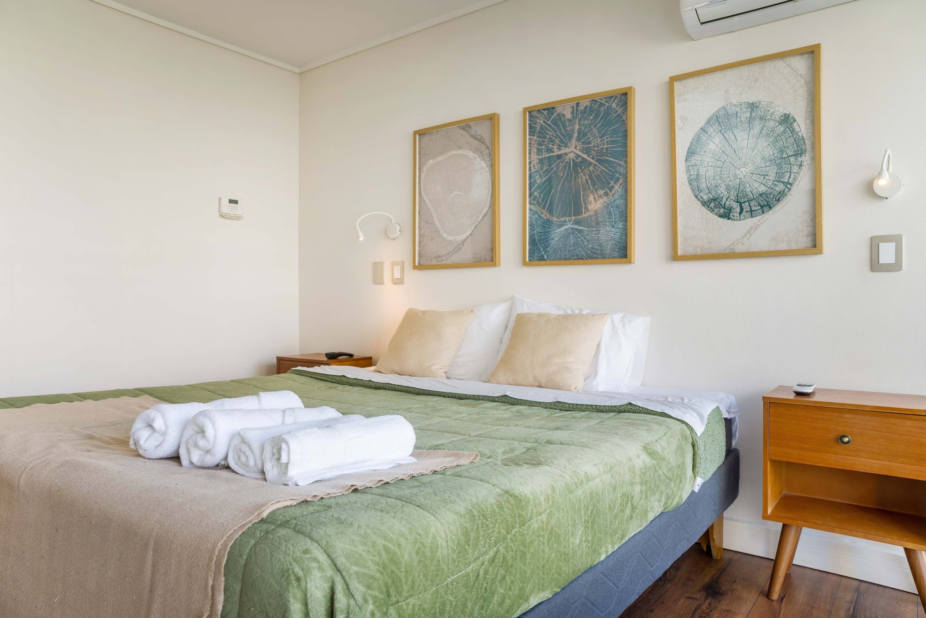 Habitación de hotel con una cama, una mesita de noche y aire acondicionado instalado en la pared.