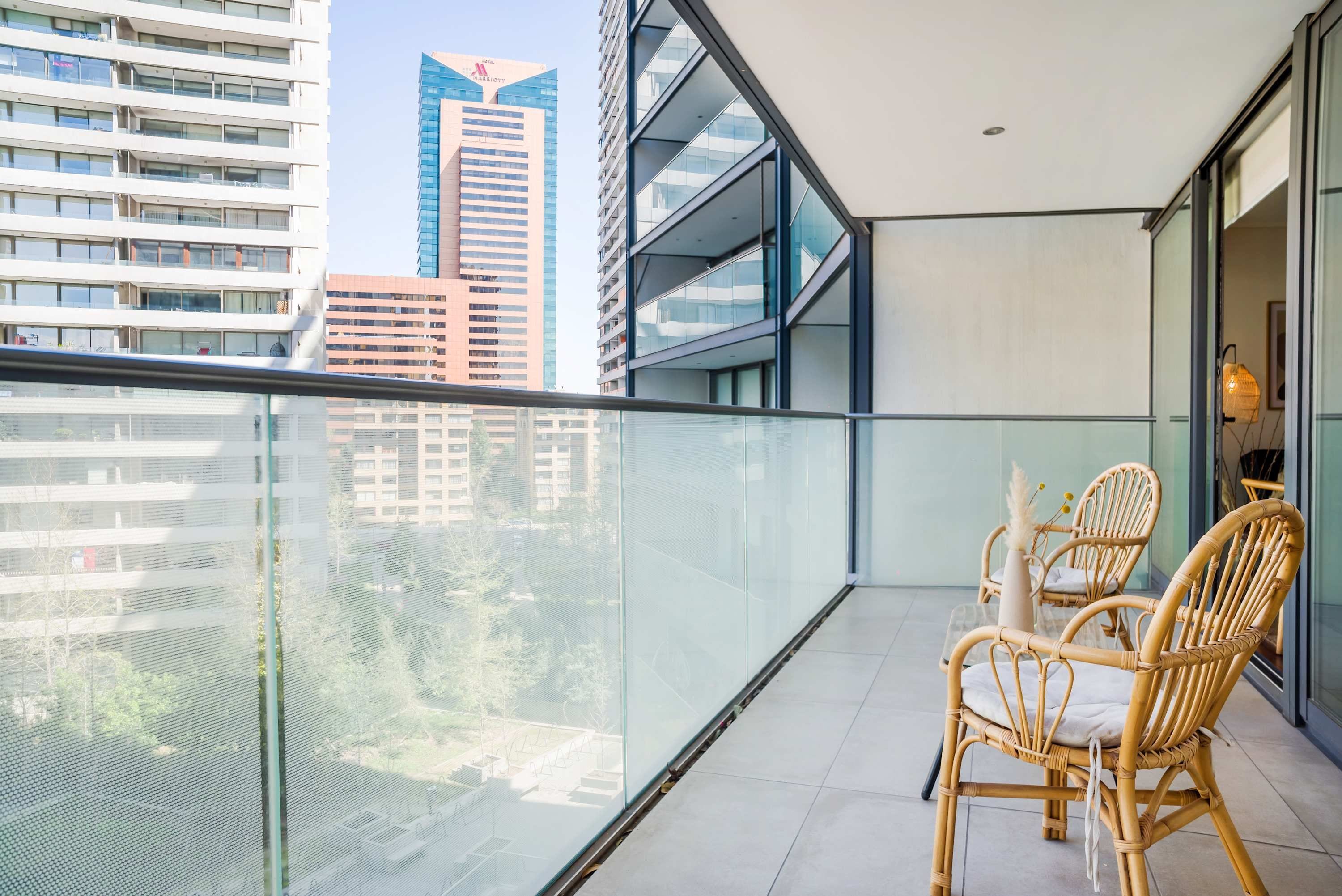 Ein Balkon mit Glasgeländer, zwei Korbstühle und Blick auf Stadtgebäude.