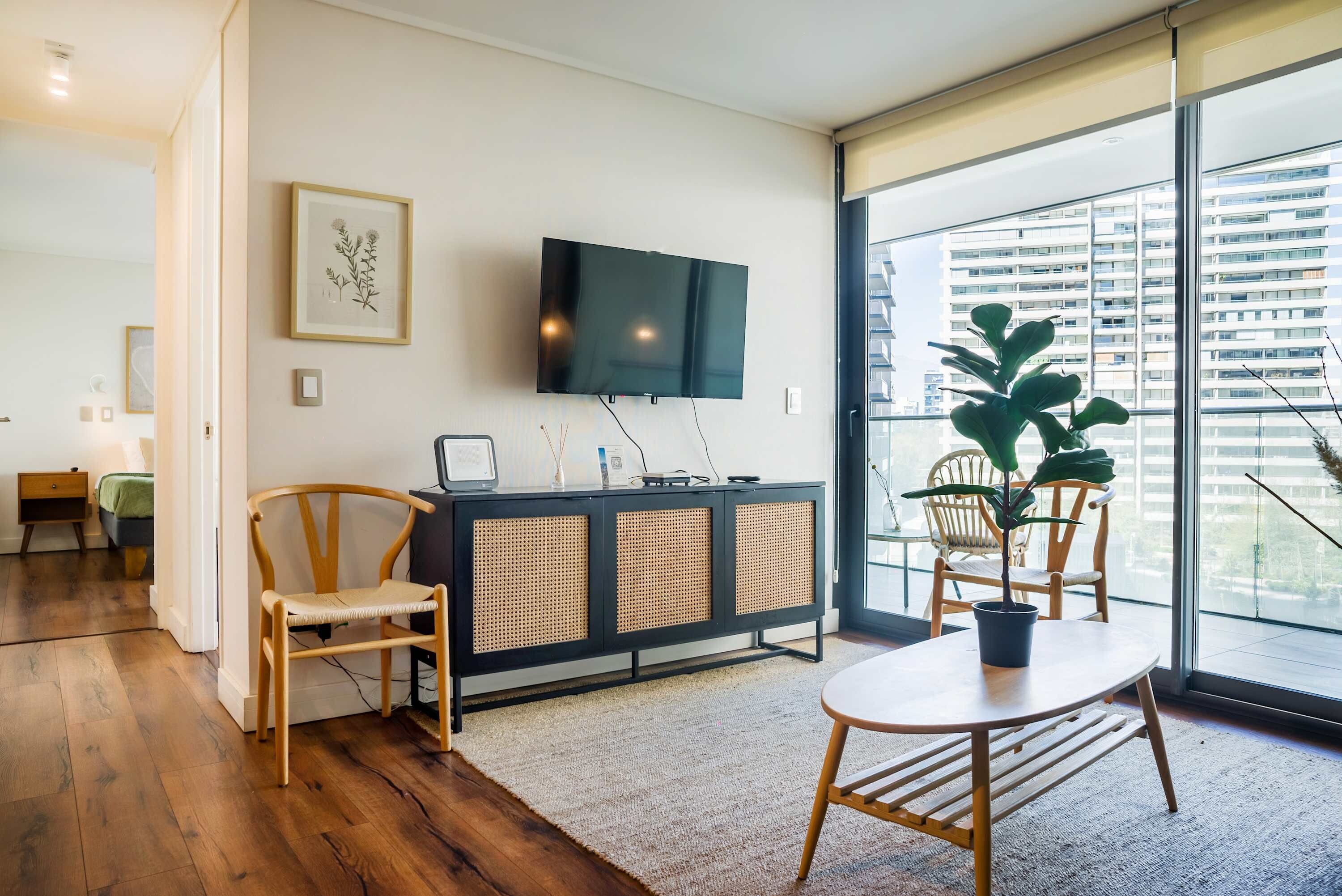 A modern living room with a flat-screen TV, wooden furniture, and a large window with a city view.