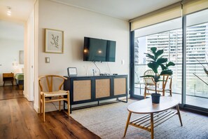 A modern living room with a flat-screen TV, wooden furniture, and a large window with a city view.