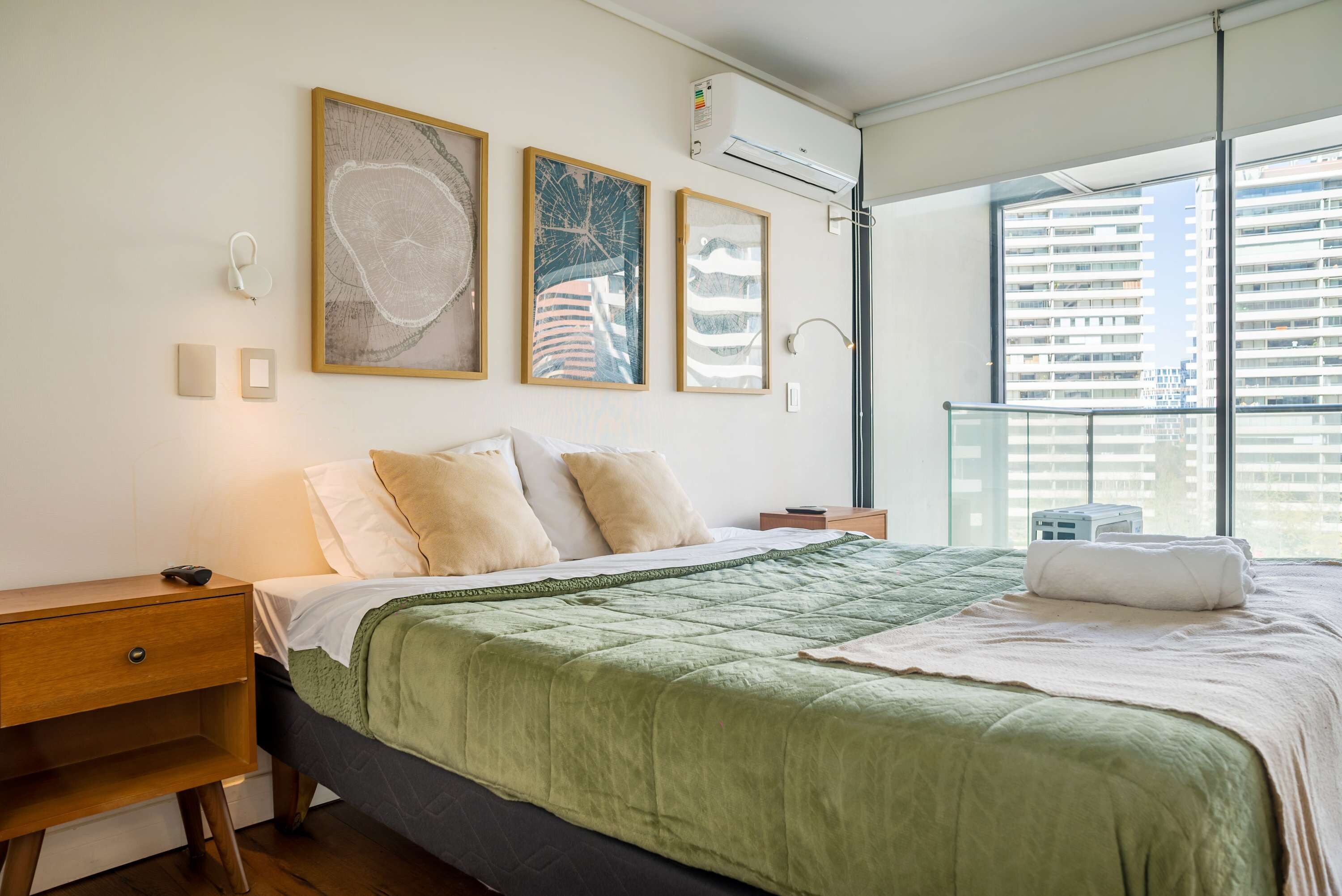 A modern bedroom with a large bed, a nightstand, a bedside table, and a window with a view of buildings.