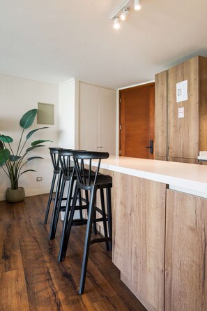 A modern kitchen with a wooden countertop, black bar stools, and a potted plant.