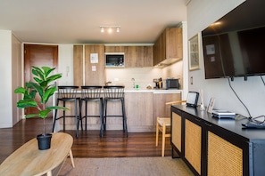 Una cocina compacta con armarios de madera, un comedor con sillas y un banco, y una planta grande en maceta.
