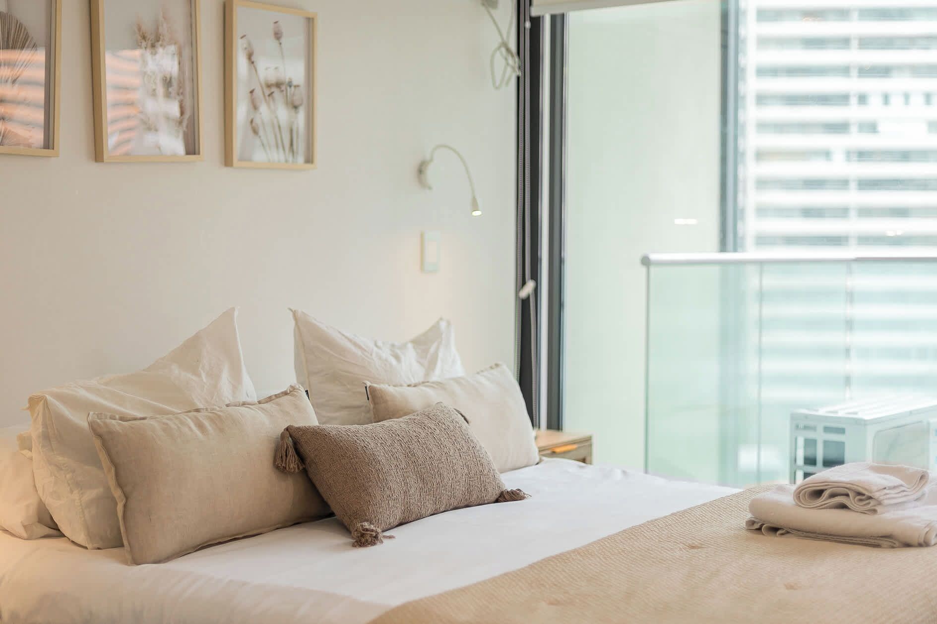 A hotel room with a bed, pillows, a blanket, and a view of the city through a window.