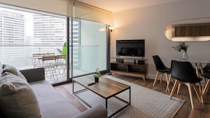 A modern living room with a sofa, coffee table, TV, and dining area. - Chic Las Condes Apt: 2BR, 2BA, Sleeps 5 (Las Condes)